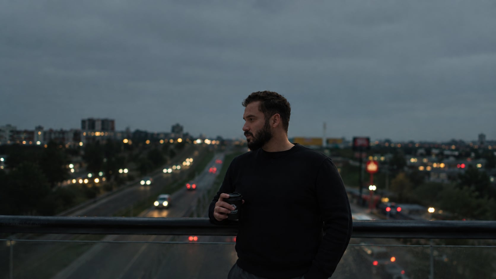 Lopes Junior em um viaduto ao entardecer, com as luzes da cidade ao fundo